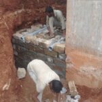 Stone masonry retaining wall construction with PVC weep holes after excavation near an existing concrete structure
