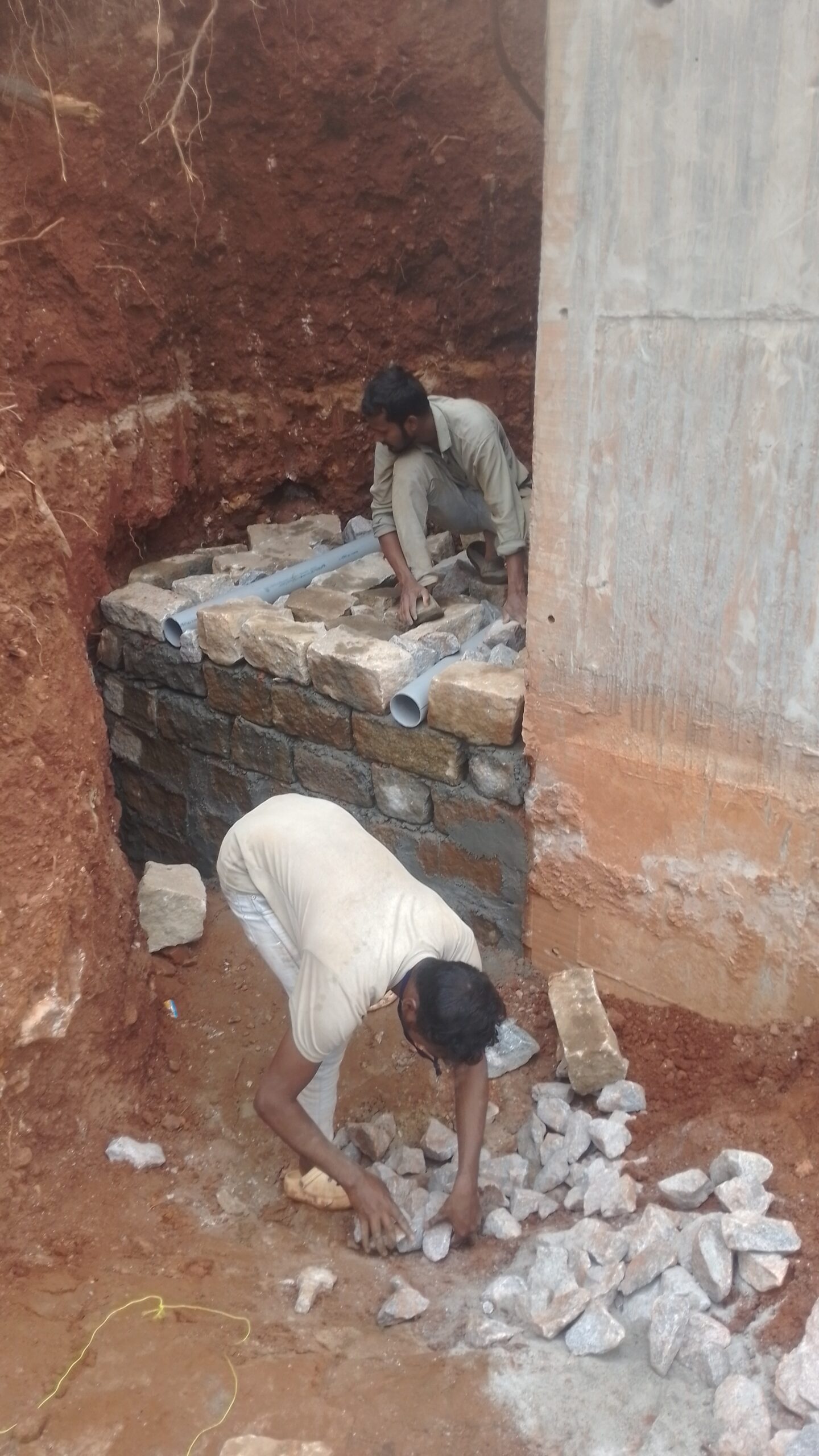 Stone masonry retaining wall construction with PVC weep holes after excavation near an existing concrete structure