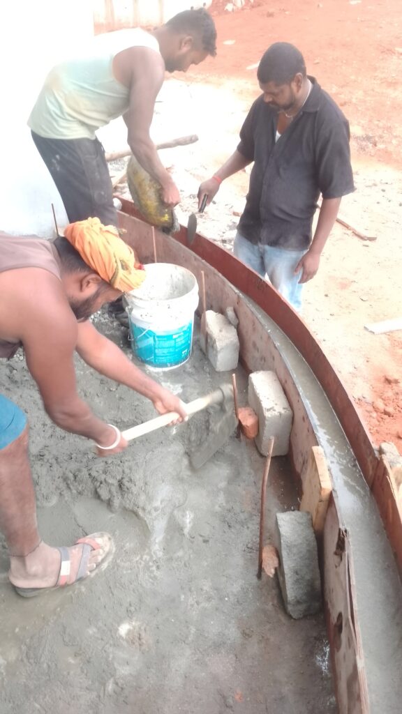 Workers carrying out curved RCC formwork concreting with steel shuttering and reinforcement at a construction site