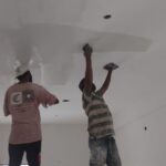 Workers applying wall putty and interior paint during building construction