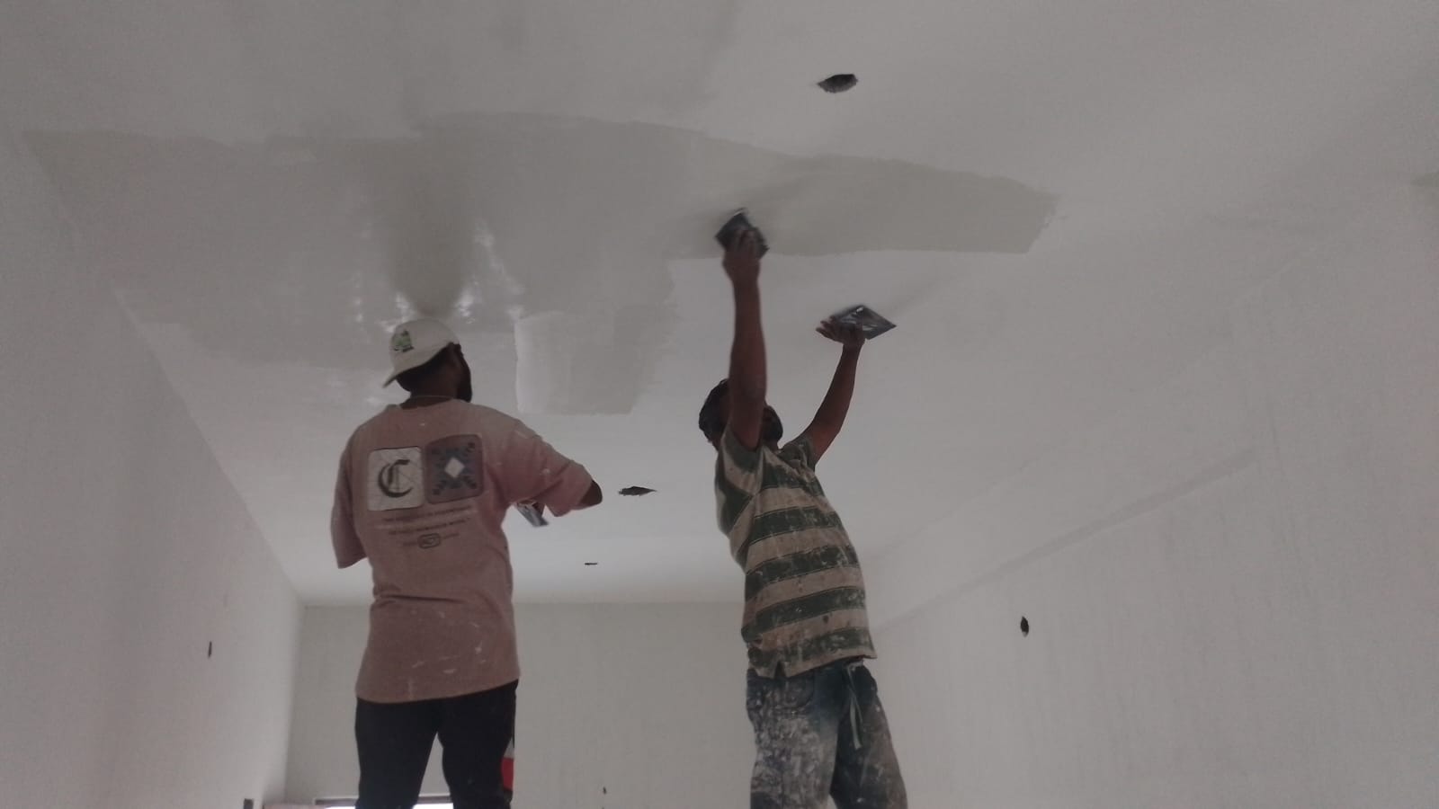 Workers applying wall putty and interior paint during building construction